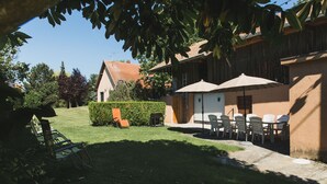 Un espace patio avec des sièges d’extérieur, une haie et un bâtiment doté d’un toit en tuiles.