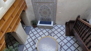 Une cour avec un sol carrelé, un escalier en bois et un mur orné de motifs.