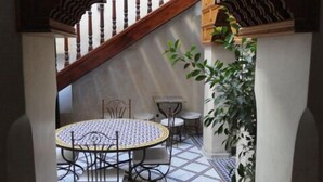 Une terrasse extérieure couverte, avec une table ronde et des chaises, un escalier avec des rampes en bois et des plantes en pot.