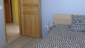 A bedroom with a wooden door, a bed with a polka dot bedspread, and a bedside lamp.