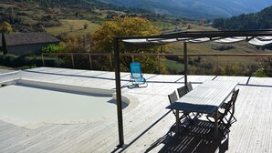 A wooden deck with a table and chairs, overlooking a mountainous landscape.
