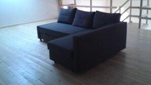 A room with a dark-colored sofa, wooden flooring, and a staircase in the background.