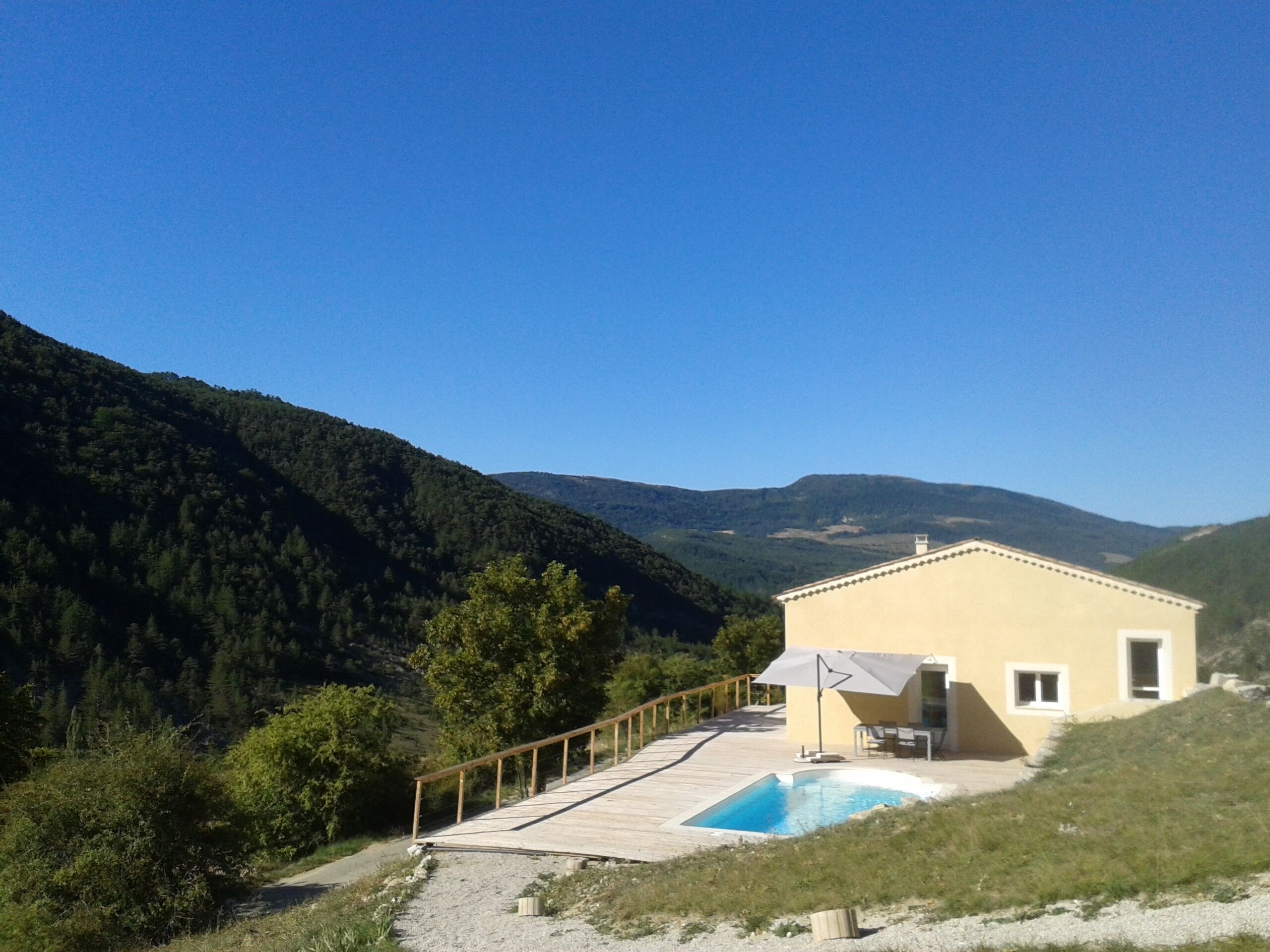 Una casa con piscina, terraza y vistas al bosque y las colinas circundantes.