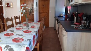 Un coin repas avec une table recouverte d’une nappe à motifs floraux, des chaises en bois et un vase rempli de fleurs.