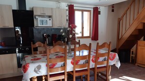 Un coin repas avec une table et des chaises en bois, un vase rempli de fleurs et, au fond, une cuisine.