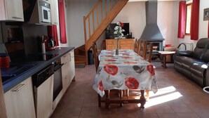 Une cuisine compacte équipée d’un four à micro-ondes, d’une cuisinière et de placards. Une table à manger avec des chaises est placée au centre de la pièce. Un escalier mène à un autre niveau.