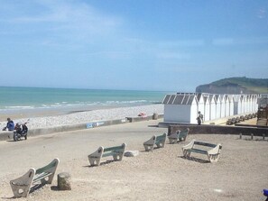 A beach with benches, a white structure, and a person walking.