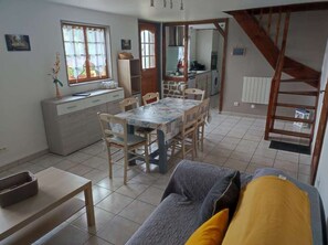 A dining area with a table and chairs, a kitchen in the background, and a staircase.