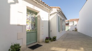 A narrow alleyway with white buildings, green shutters, and potted plants. - Island of Re. House near sandy beach, harbor and shops (La Flotte)