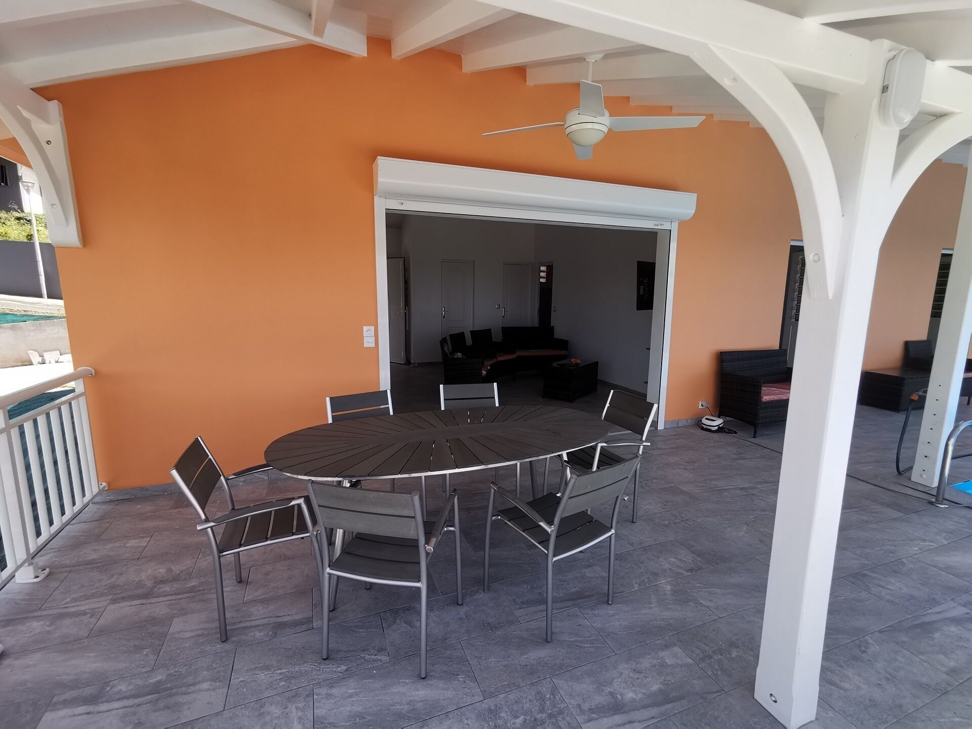 An outdoor patio with a round table and chairs, a ceiling fan, and a view of the interior.