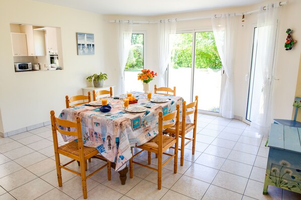 A dining area with a table set for four, surrounded by wooden chairs, a tiled floor, and a view through a glass door to the outside.