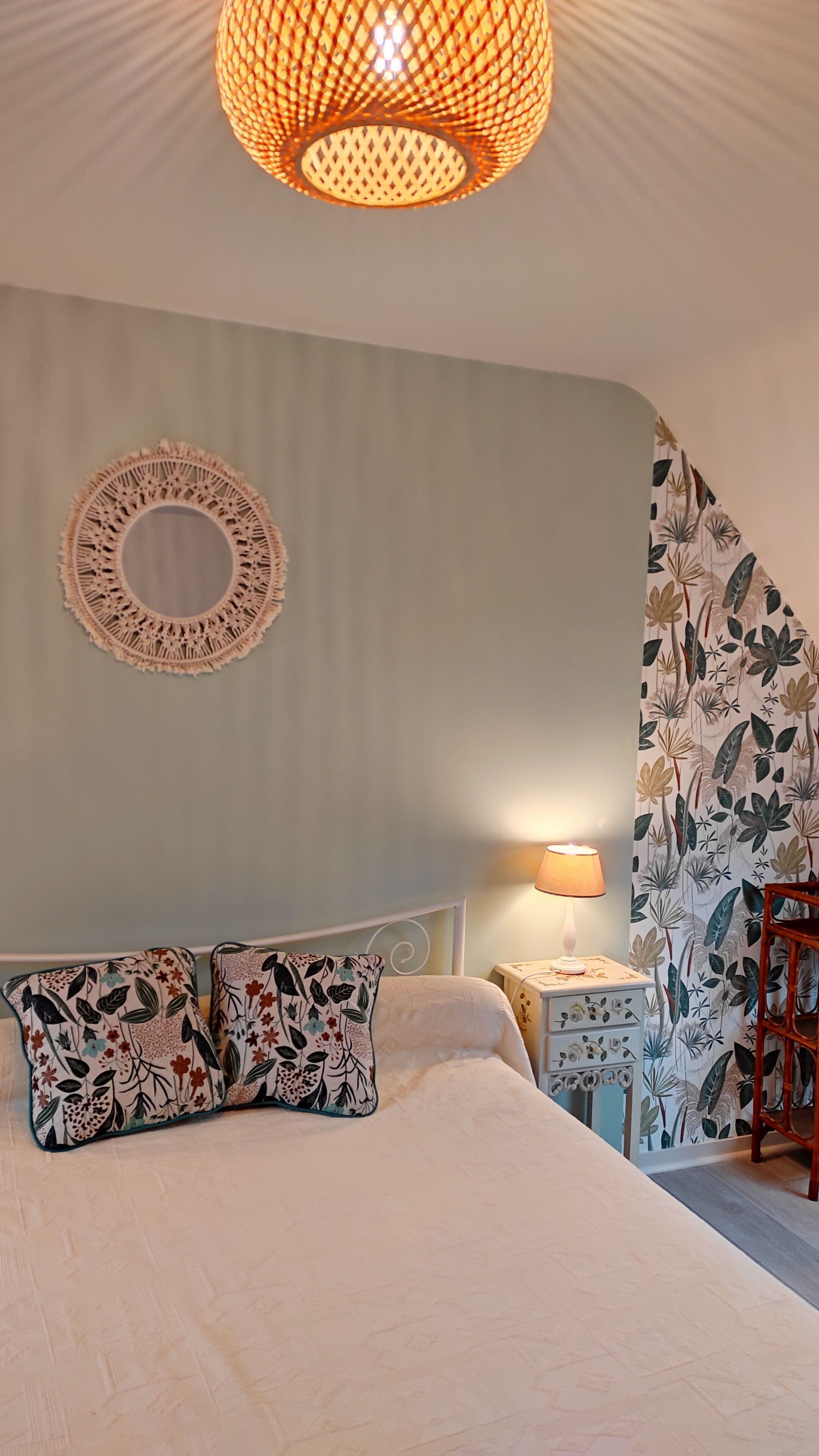 A bedroom with a bed, a round wall hanging, a patterned wall, and a hanging light fixture.
