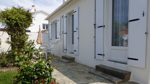 A white building with shuttered windows, a stone-paved courtyard, and a small garden with roses.