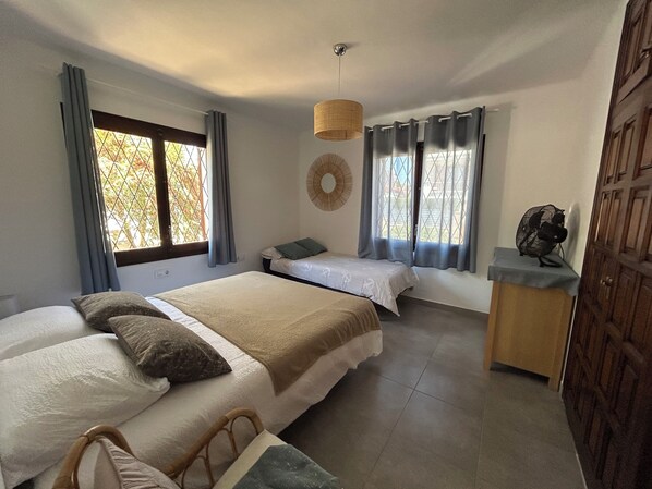 Une chambre avec deux lits, une petite table, un ventilateur et une porte.