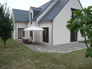 A modern house with a patio, a dining table with chairs, and a large umbrella. - New house in Piriac sur mer, small town of character by the sea (Piriac-Sur-Mer)