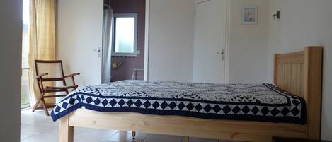 Een slaapkamer met een bed, houten hoofdbord, een stoel, een klein tafeltje en een deur naar een badkamer.