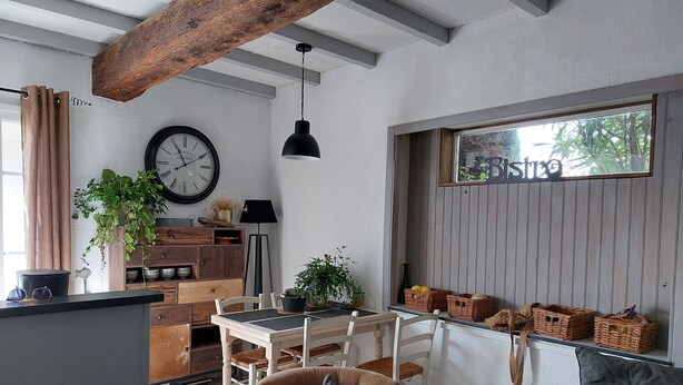 A cozy living room with a dining area, wooden ceiling beams, a clock, and a window with a view of trees. - THE FLEET IN RE classified ** (La Flotte)