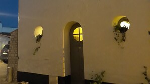 A two-story building with a white facade, two windows with illuminated interiors, and a central arched doorway. - THE FLEET IN RE classified ** (La Flotte)