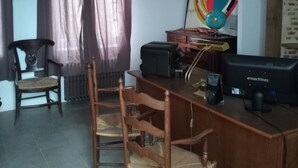 A room with a wooden desk, two chairs, a radiator, a black suitcase, a computer, and a colorful abstract painting on the wall. - Gite in Normandy with private and heated swimming pool. (Bacqueville-En-Caux)