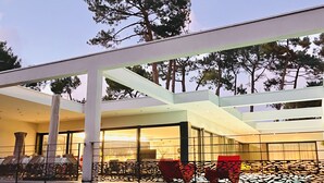 Une terrasse extérieure moderne, dotée d’une véranda en verre, de chaises rouges et offrant une vue sur les arbres.