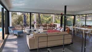 Un vaste espace de vie comprenant un grand canapé, une table à manger et un coin cuisine visible à travers de grandes fenêtres.