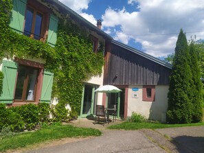 Un bâtiment avec des volets verts, un espace extérieur abrité avec des sièges, et une enseigne indiquant qu’il s’agit d’un restaurant.
