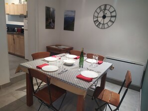 Un coin repas avec une table dressée pour quatre personnes, une horloge au mur et une vue sur la cuisine.