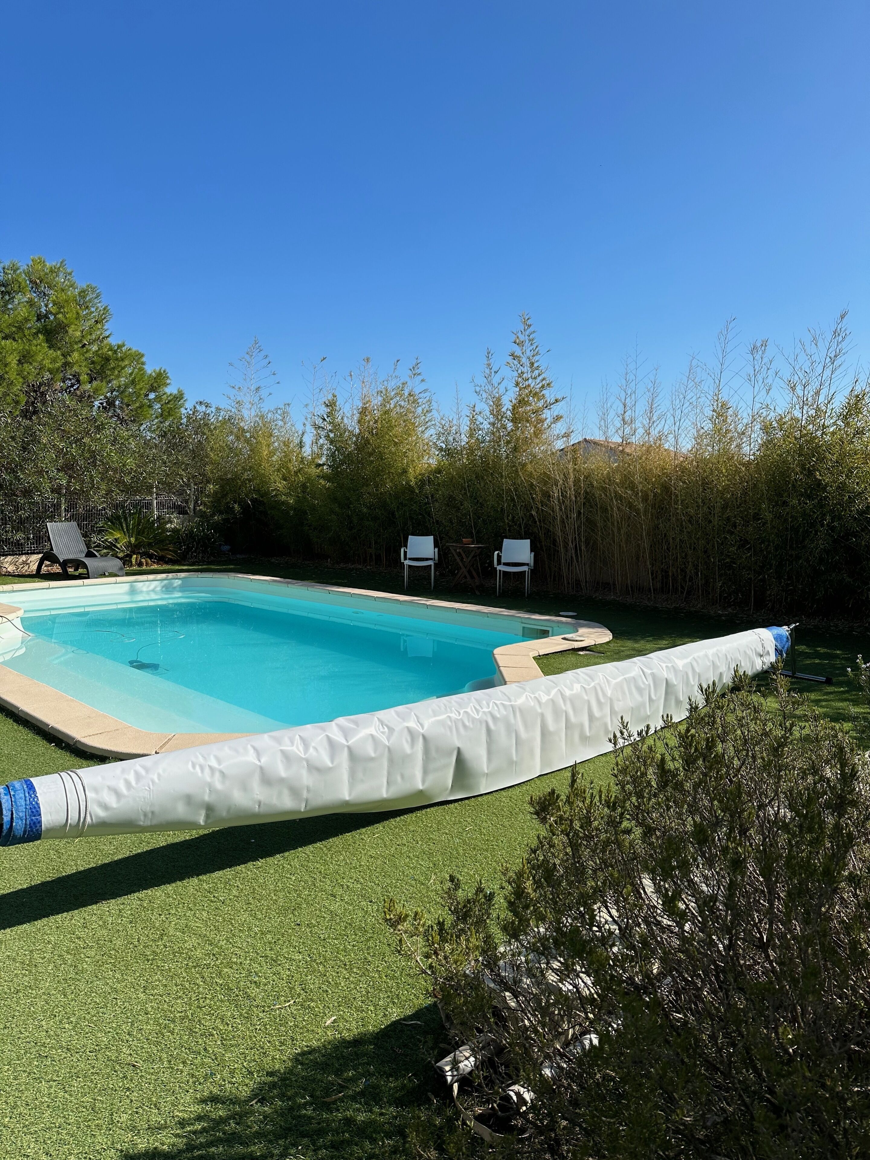 Ein rechteckiger Pool mit weißer Abdeckung, umgeben von Rasen und Bäumen.