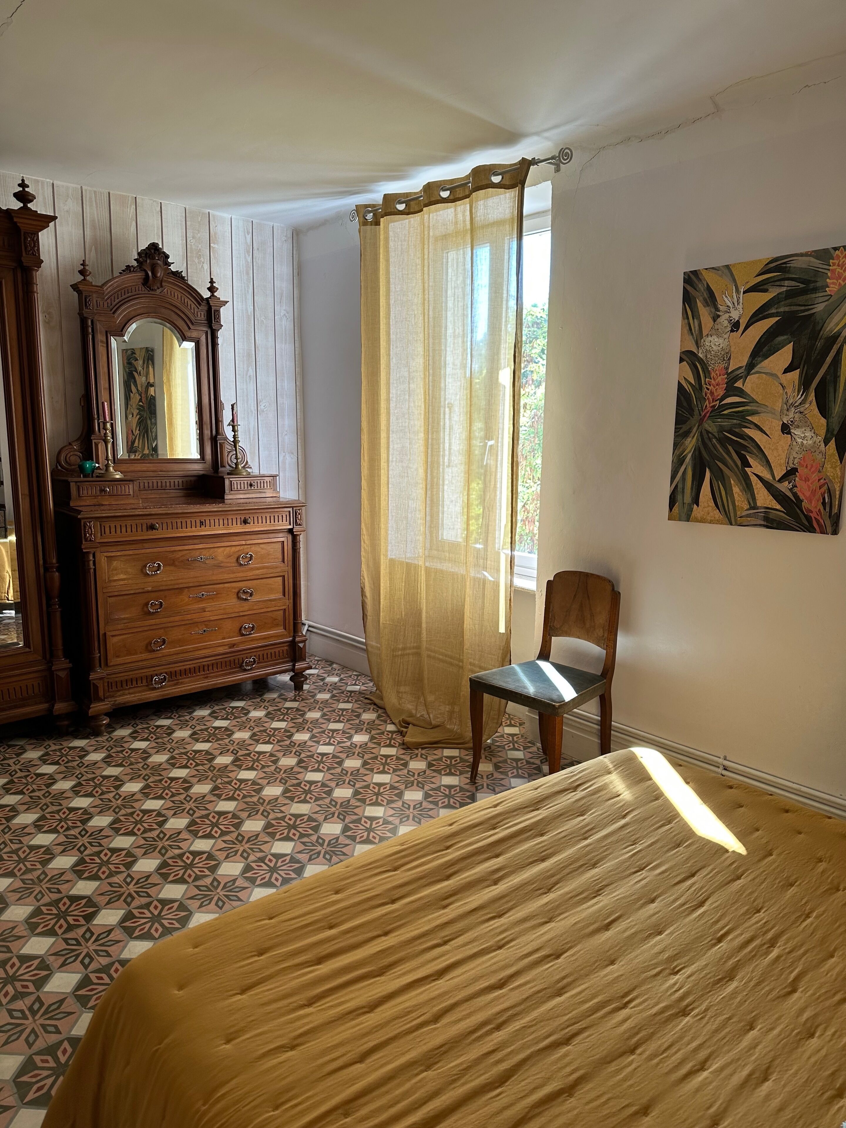 A bedroom with a bed, a wooden dresser, a chair, and a painting on the wall.