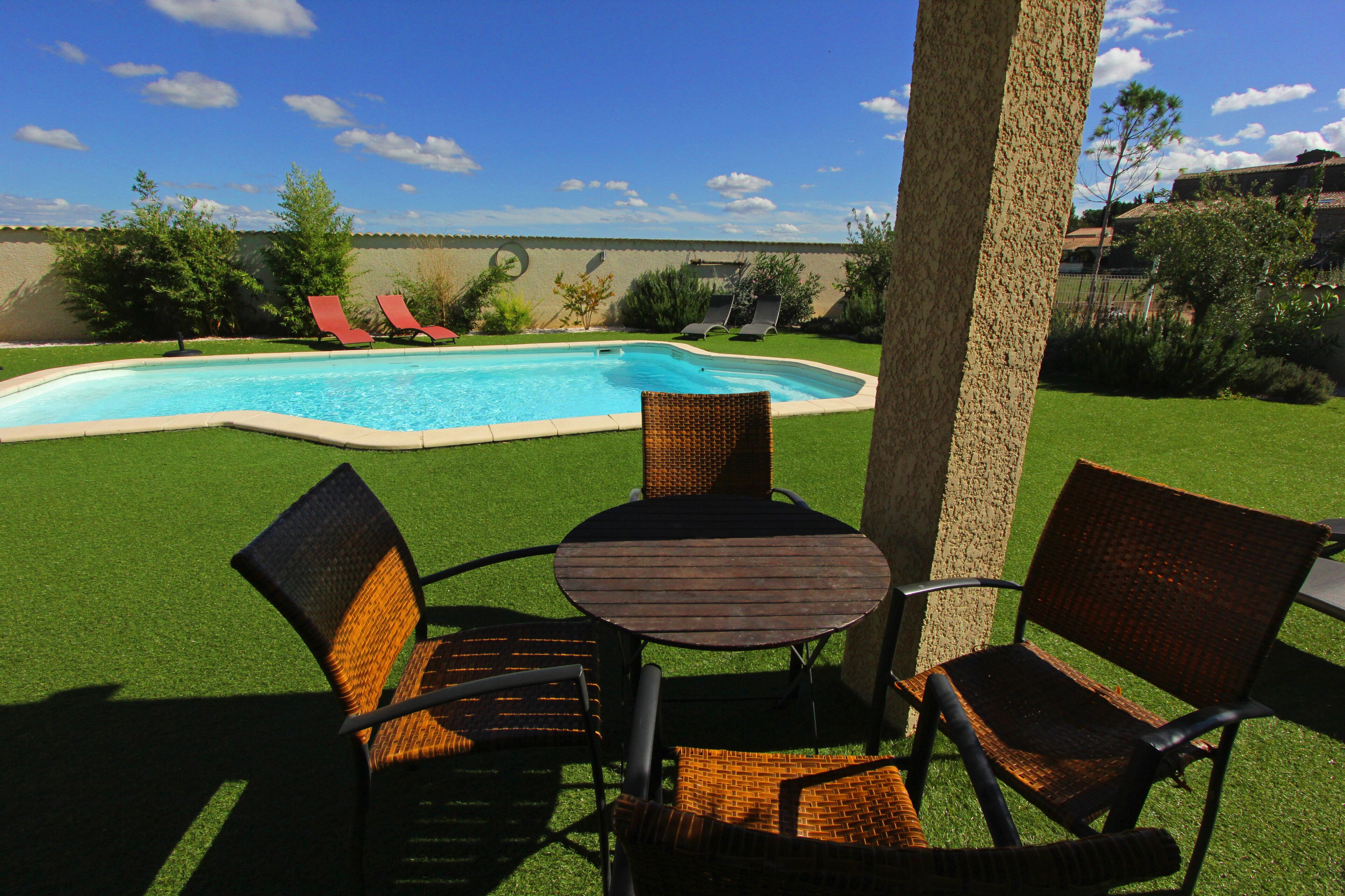 Un jardin avec une piscine, une pelouse verdoyante et du mobilier d’extérieur comprenant une table et des chaises.