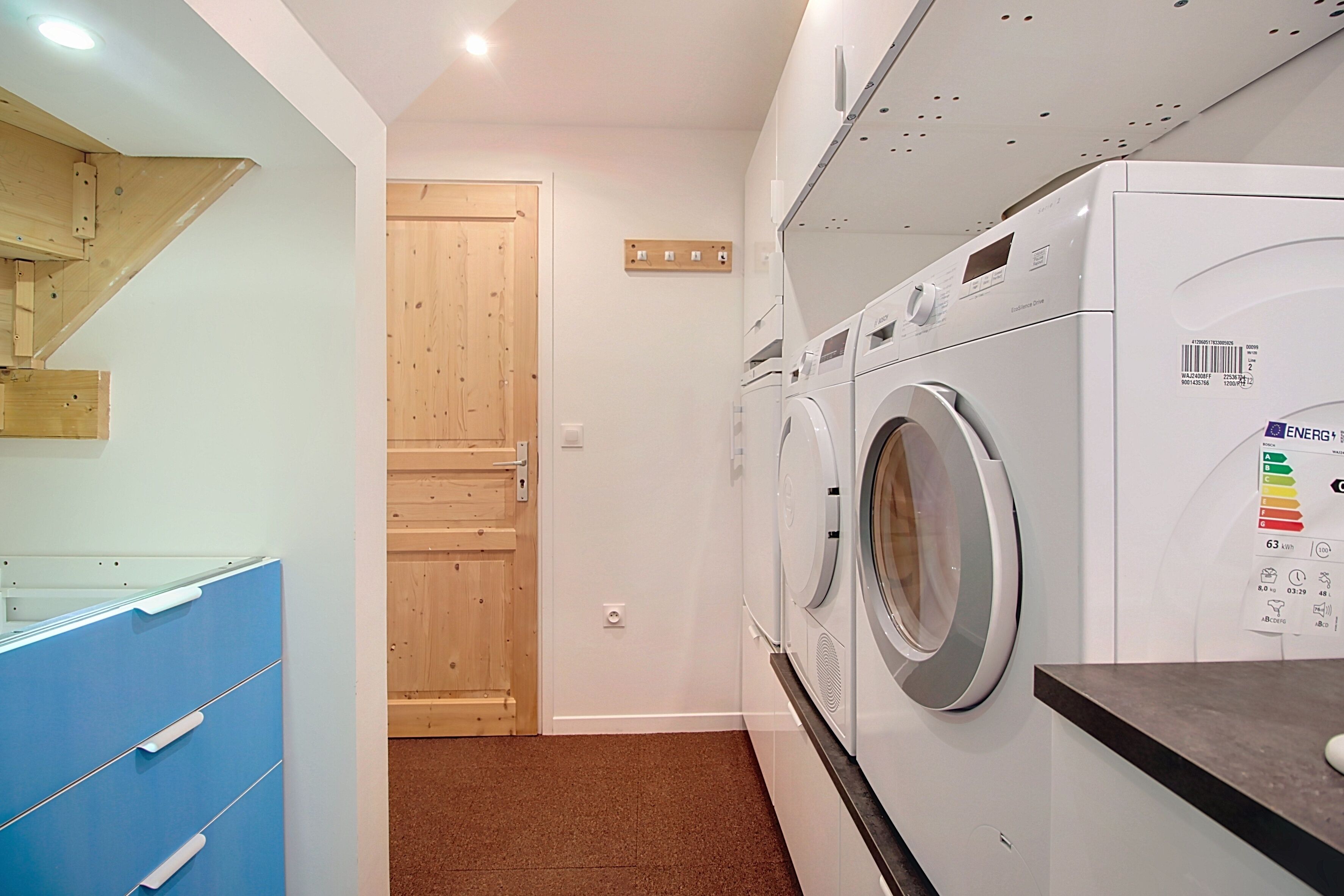 A laundry room with a washing machine and dryer, wooden door, and blue storage unit.
