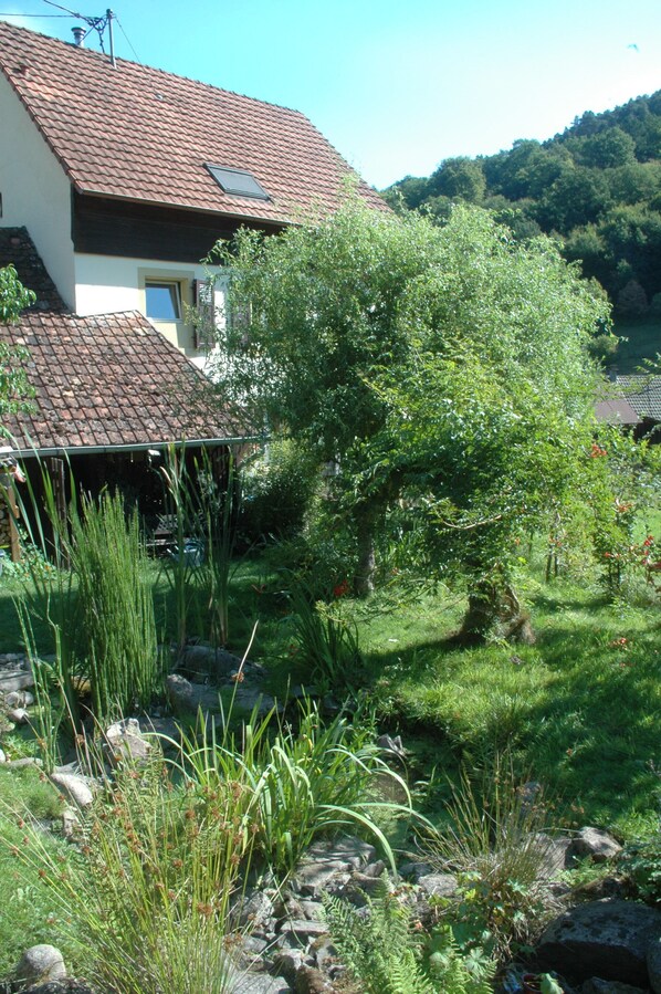 A house with a tiled roof, surrounded by a garden with various plants and a small pond.