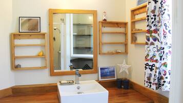 Un baño con tocador de madera, un lavabo blanco, un espejo y estantes con diversos objetos.