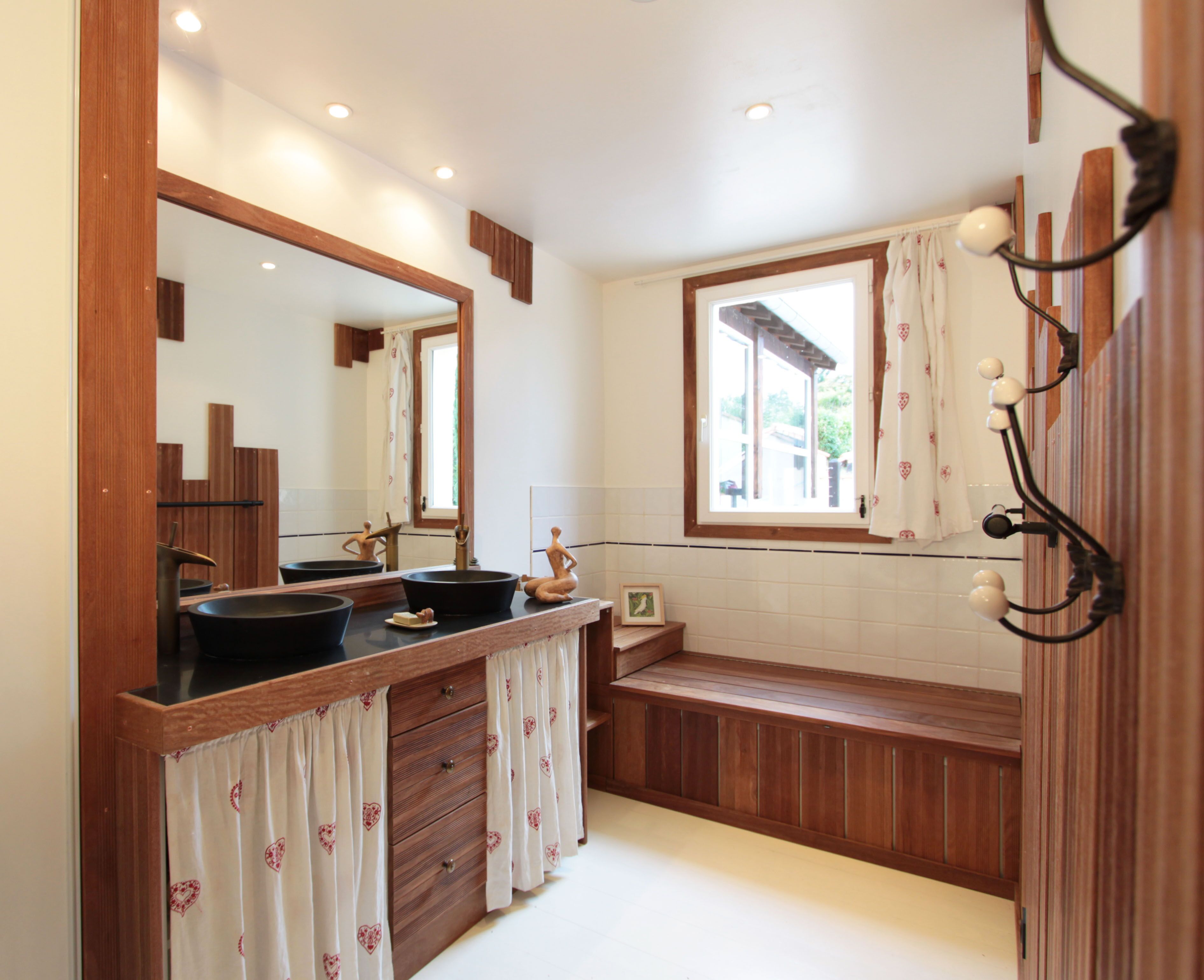 A bathroom with wooden vanity, two sinks, a mirror, and a window with curtains.