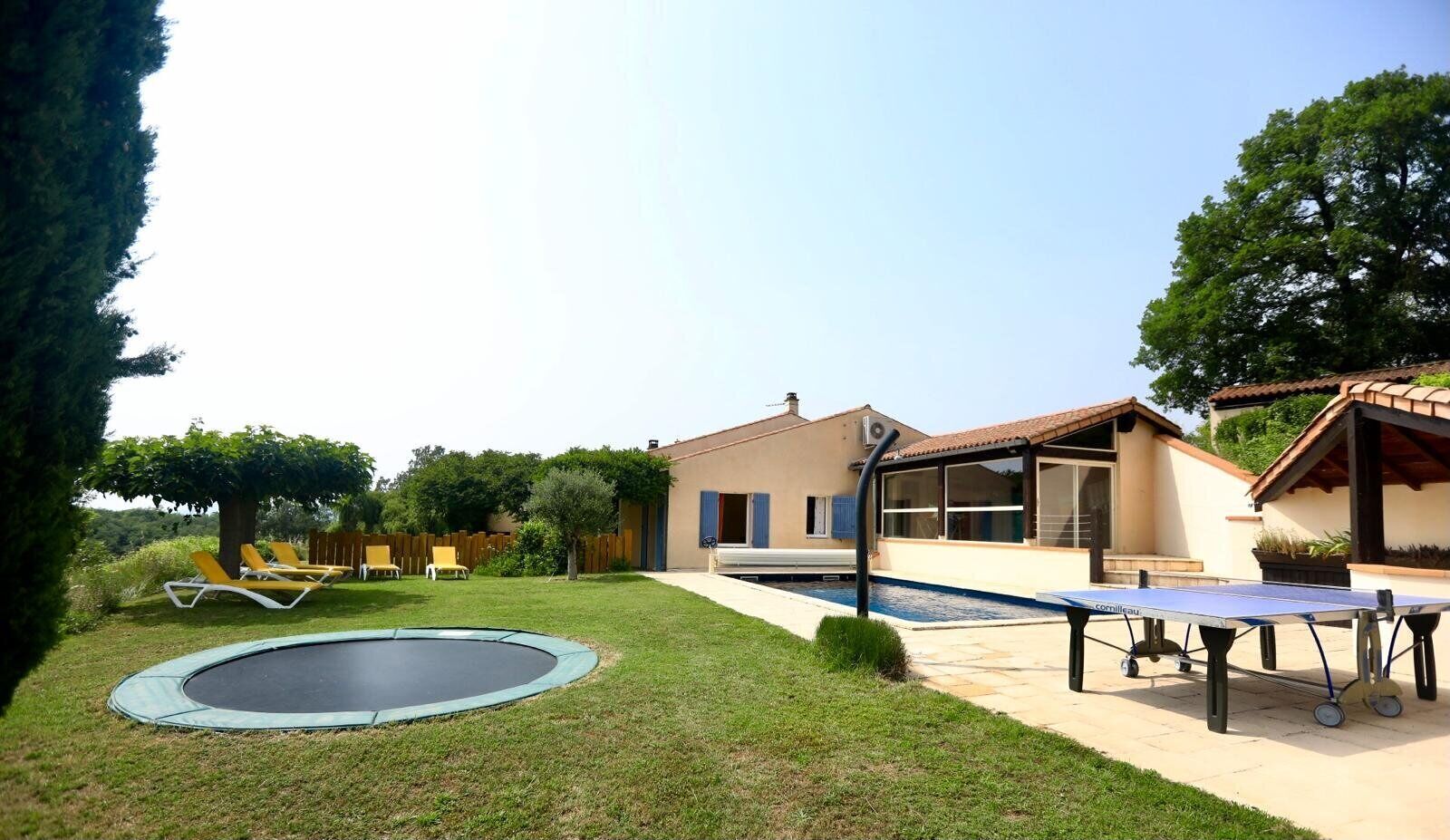 A backyard with a trampoline, a pool table, and a house with a patio.