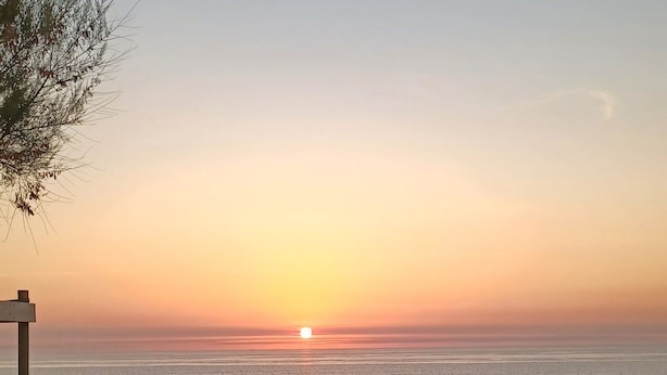 Une plage au coucher du soleil, un sentier de sable et un panneau indicateur.