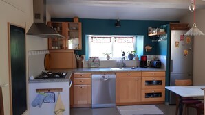 A compact kitchen with wooden cabinets, a built-in dishwasher, a gas stove, and a window with decorative curtains. - VERY NICE HOUSE WITH LUBERON POOL (Cavaillon)