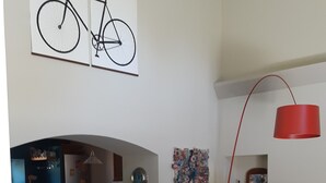 A modern living room with a sofa, coffee table, and a dining area with a table and chairs. There is a kitchen area with cabinets and a refrigerator. A bicycle is mounted on the wall above the sofa. - VERY NICE HOUSE WITH LUBERON POOL (Cavaillon)