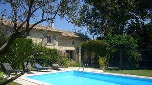 A swimming pool with lounge chairs, a stone building with a tiled roof, and surrounding greenery. - VERY NICE HOUSE WITH LUBERON POOL (Cavaillon)