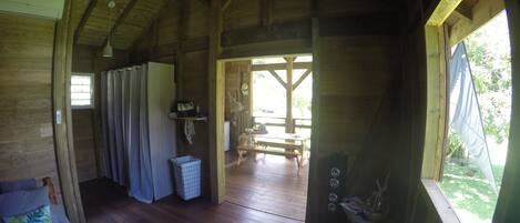 A wooden cabin interior with a bed, a table, and a view of the outdoors.