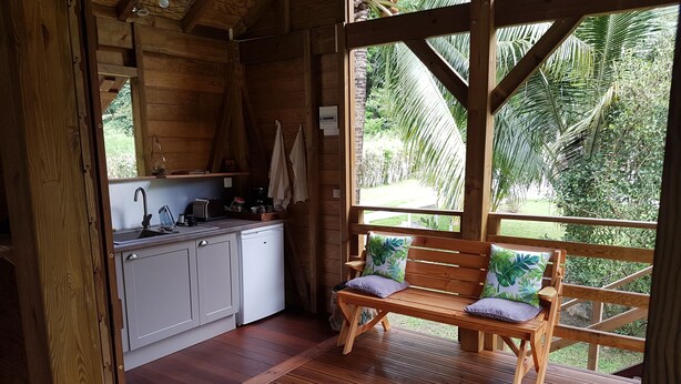 Una cabaña de madera con cocina, un banco de madera con cojines y vistas a un follaje exuberante.