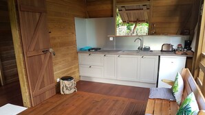 Una cocina compacta con un lavamanos, un refrigerador pequeño y una zona de comedor de madera con un banco y cojines.