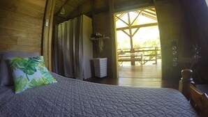 Interior de madera con una cama, un banco y vistas al exterior.