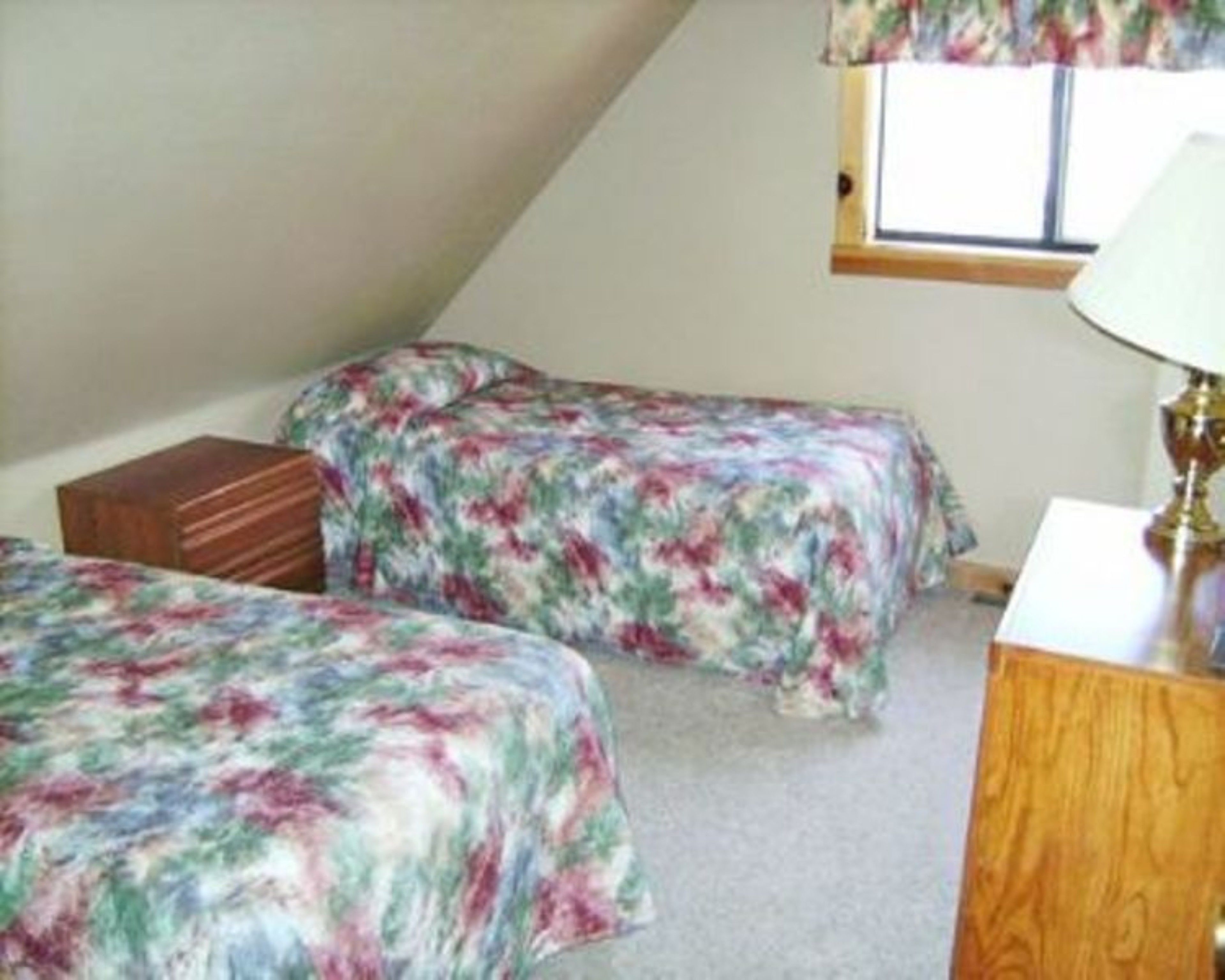 A bedroom with two beds, a window, and a lamp.