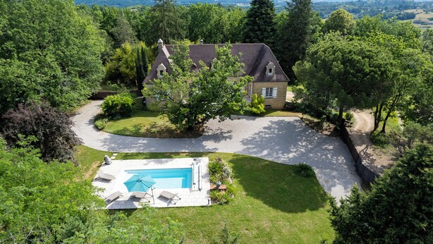 Une maison avec une piscine, entourée d’arbres et dotée d’une pelouse bien entretenue.