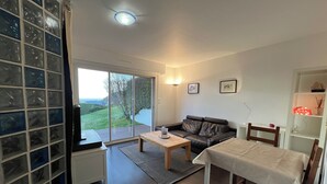 A cozy room with a sofa, a small table, a dining table, and a view of the outdoors through a sliding door. - Beautiful view of the port and the Verdelet. Garden level. Wifi   (Erquy)