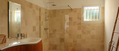 Un baño con ducha, lavamanos, espejo y ventana.
