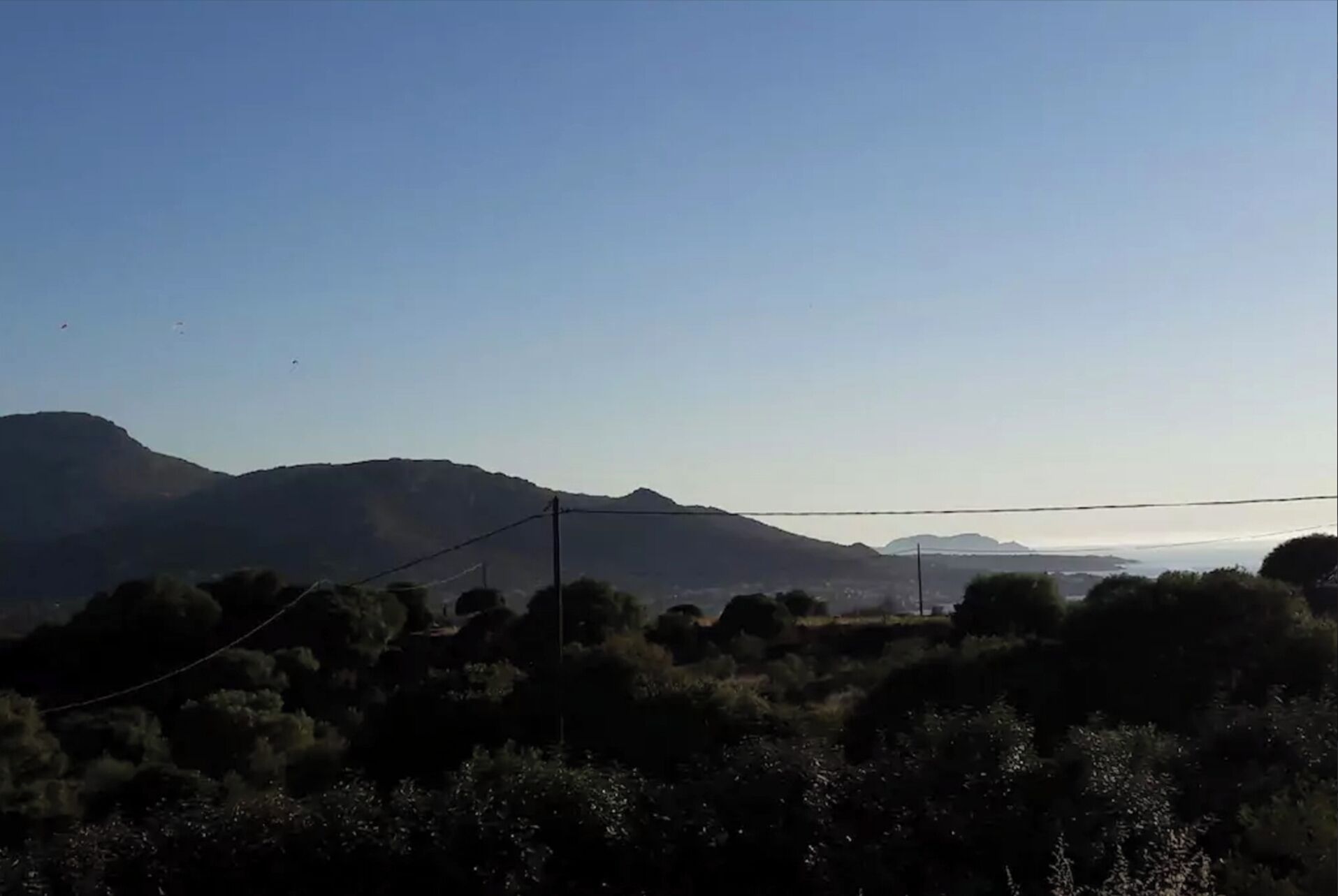 A landscape with mountains, power lines, and dense vegetation.