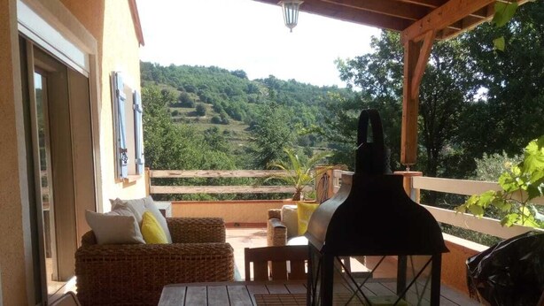 A wooden deck with a table and chairs, a wicker sofa, and a lantern. - Villa with private pool in a quiet location with mountain views 5 min from Ceret (reynes)
