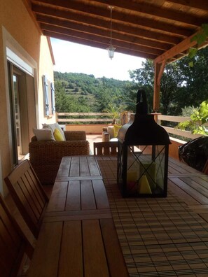 A wooden deck with a table and chairs, a wicker sofa, and a lantern. - Villa with private pool in a quiet location with mountain views 5 min from Ceret (reynes)